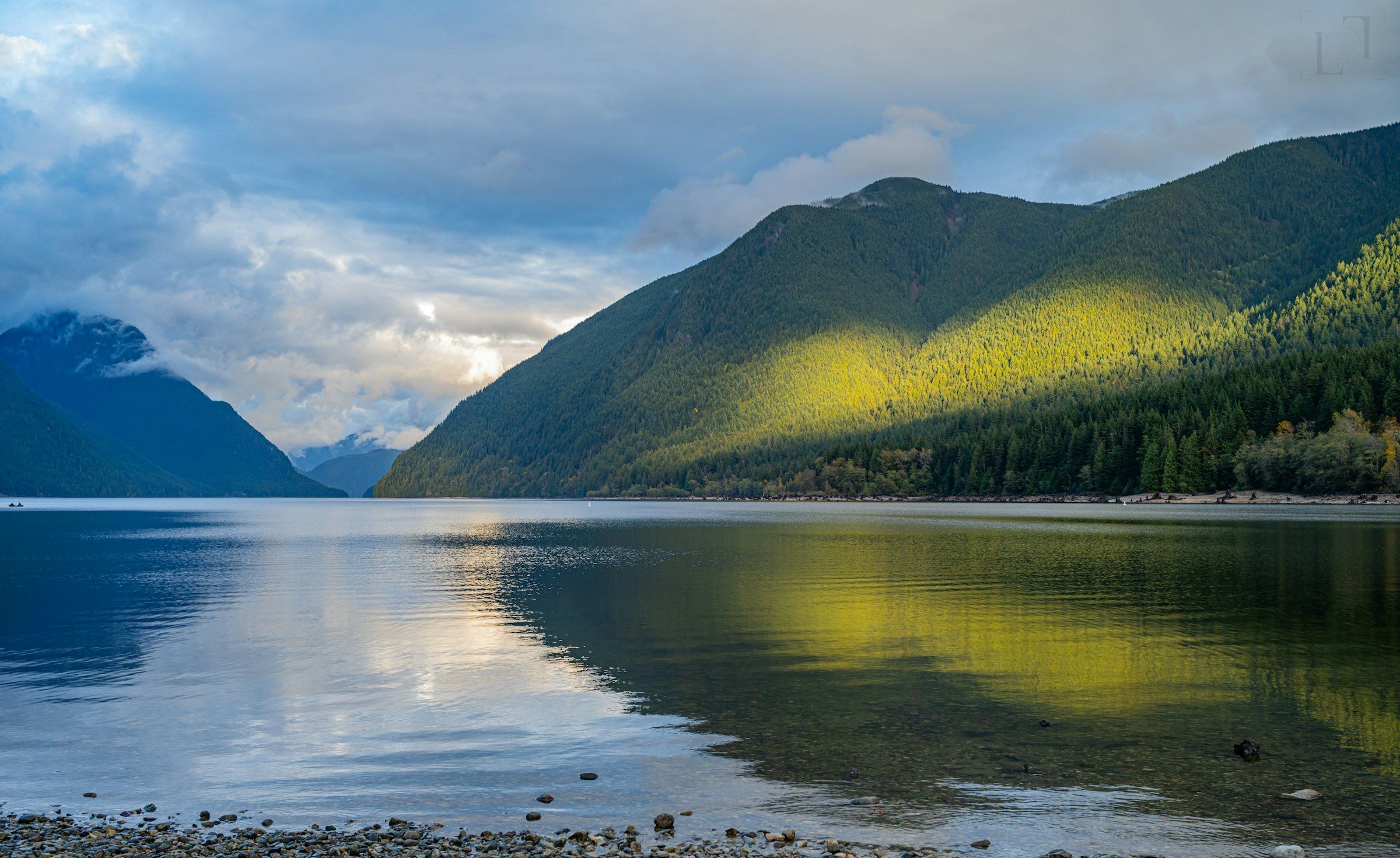 A lake in British Columbia ringed by forested mountains under broken cloud