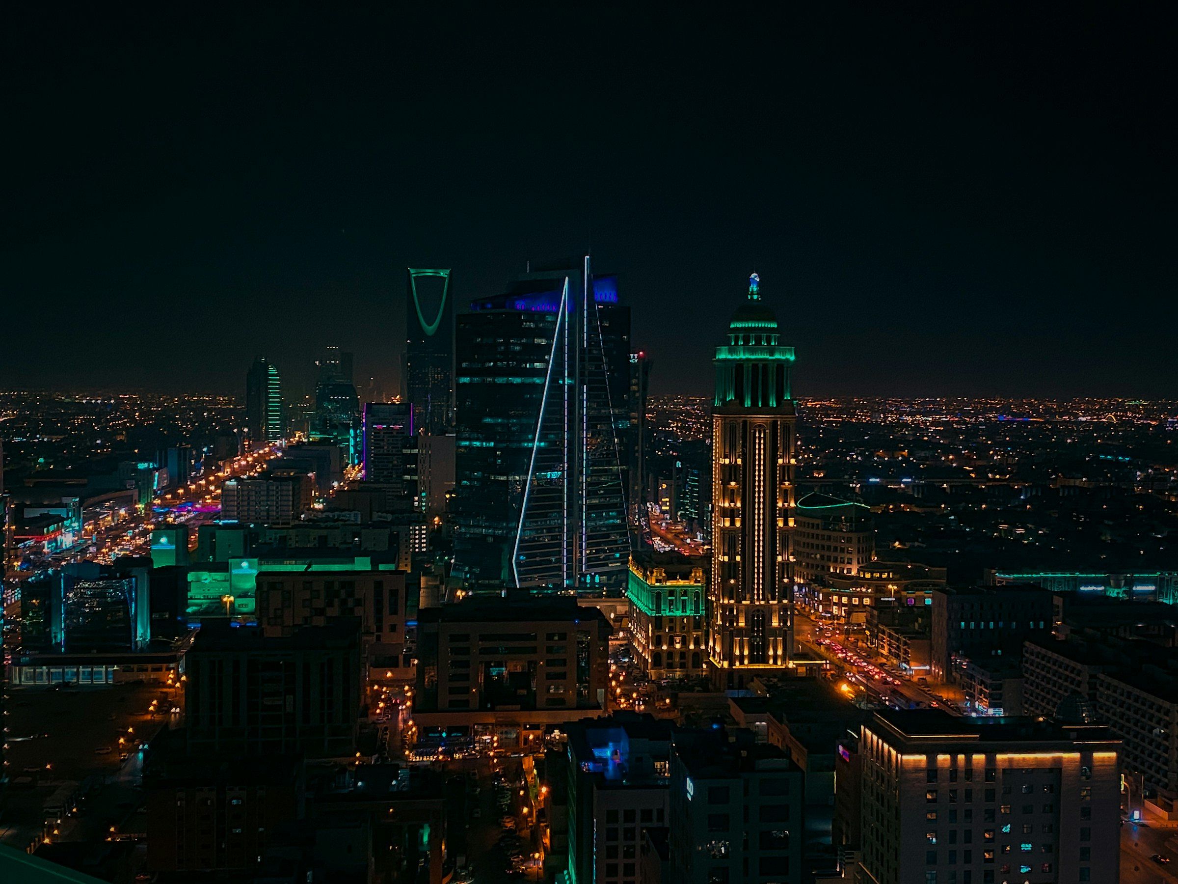 A Saudi city skyline at night, high-rise towers lit above dense low-rise blocks and traffic