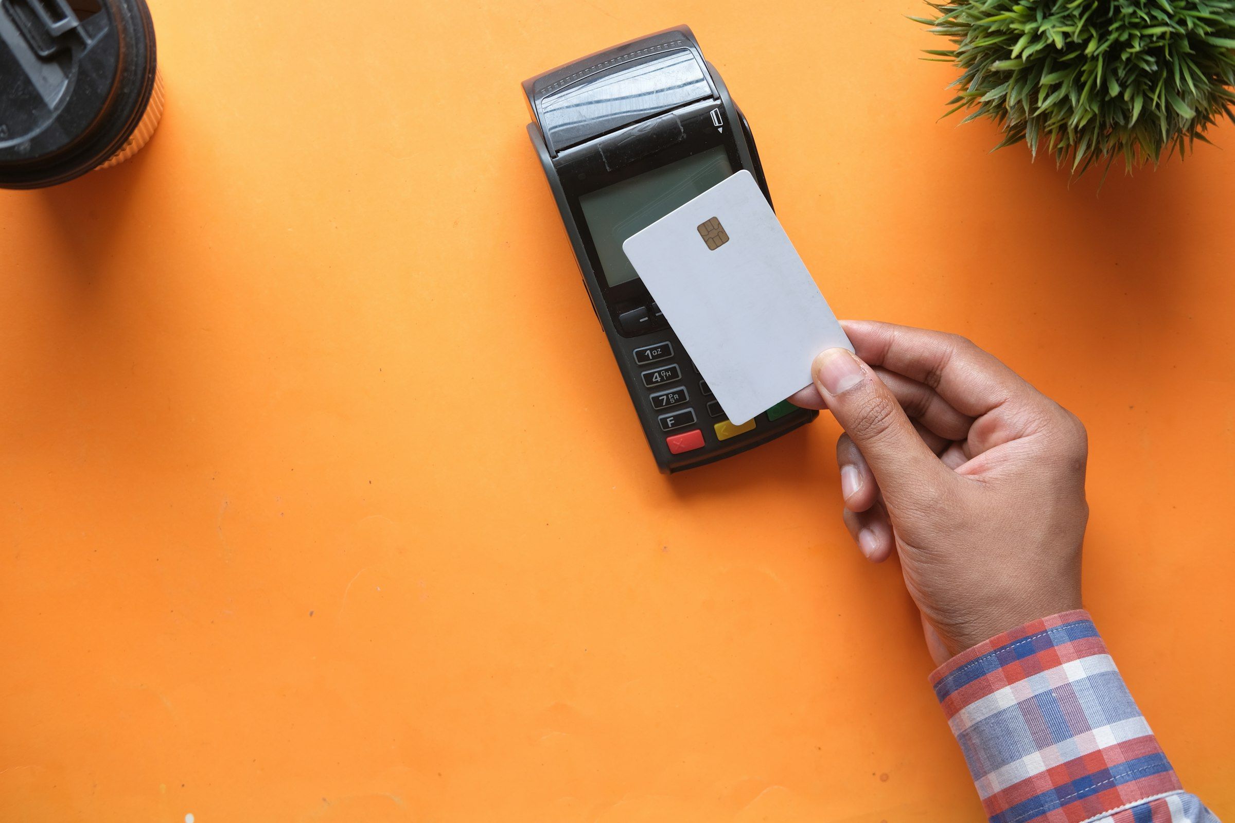 Overhead view on an orange background of a hand holding a plain white unmarked chip card against a black card-payment terminal