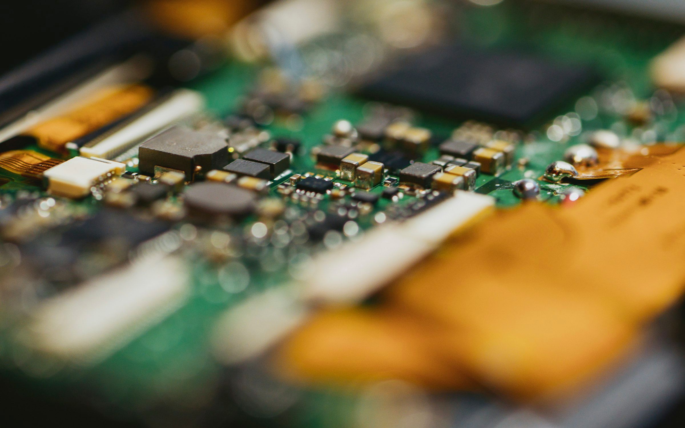 Close-up of a green circuit board with surface-mounted components and gold-toned ribbon connectors, shallow depth of field