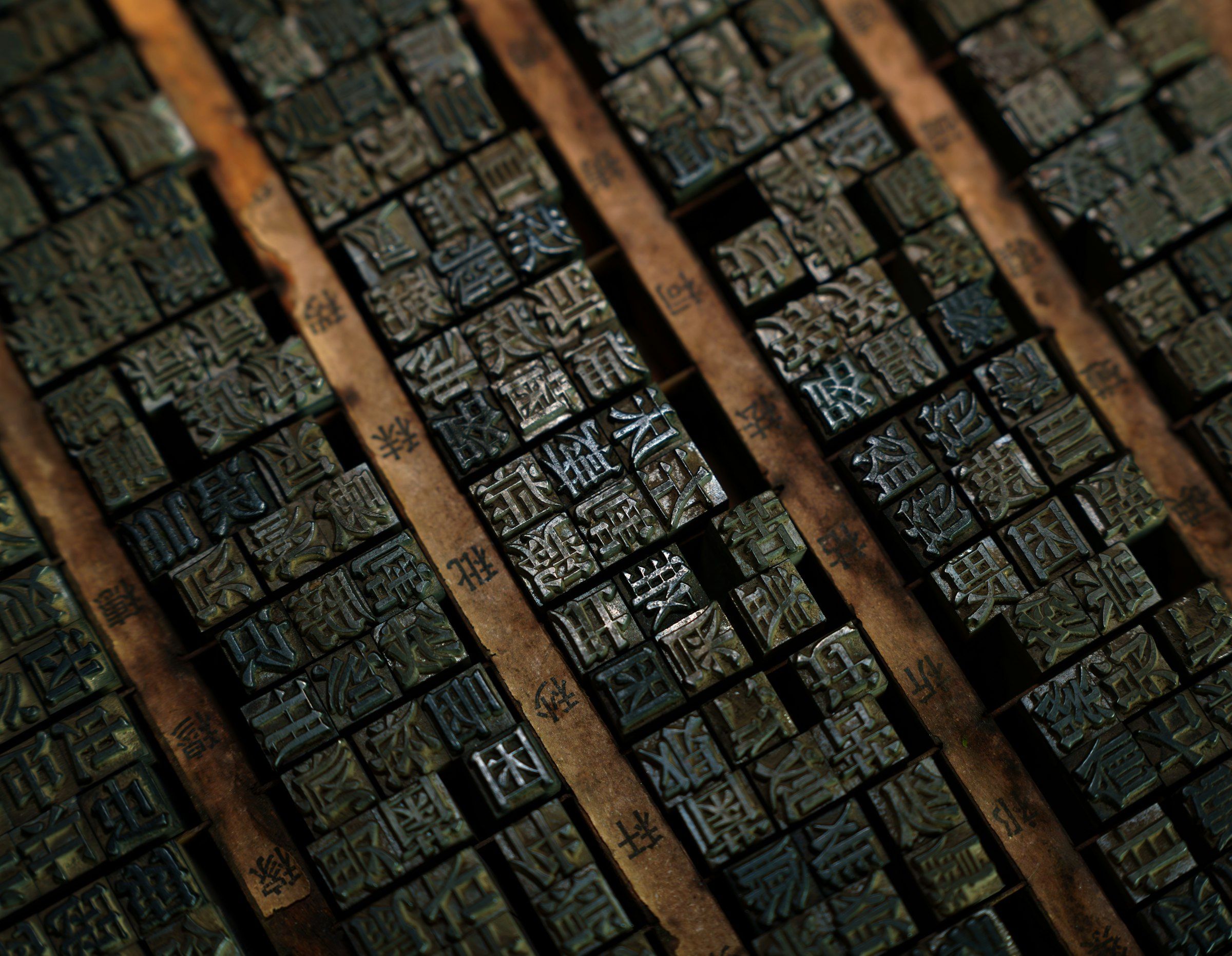 Close-up of rows of small metal letterpress type blocks packed into wooden composing trays, each block carrying a single raised character