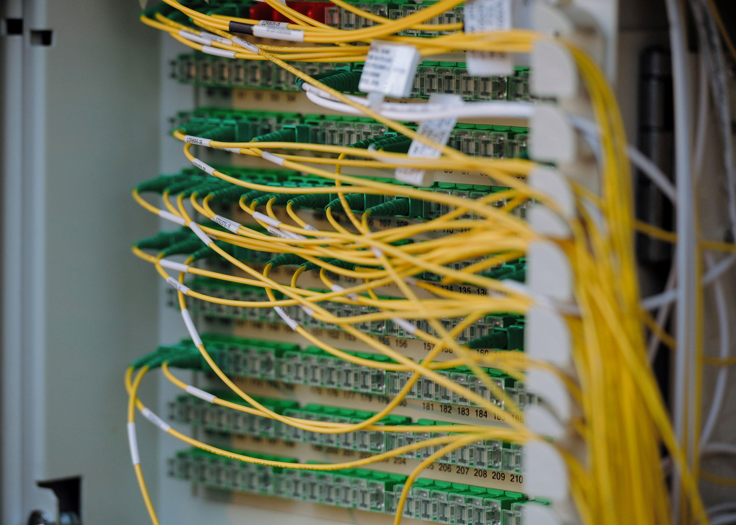 Yellow fibre-optic patch cords crossing between green connectors on a numbered termination panel