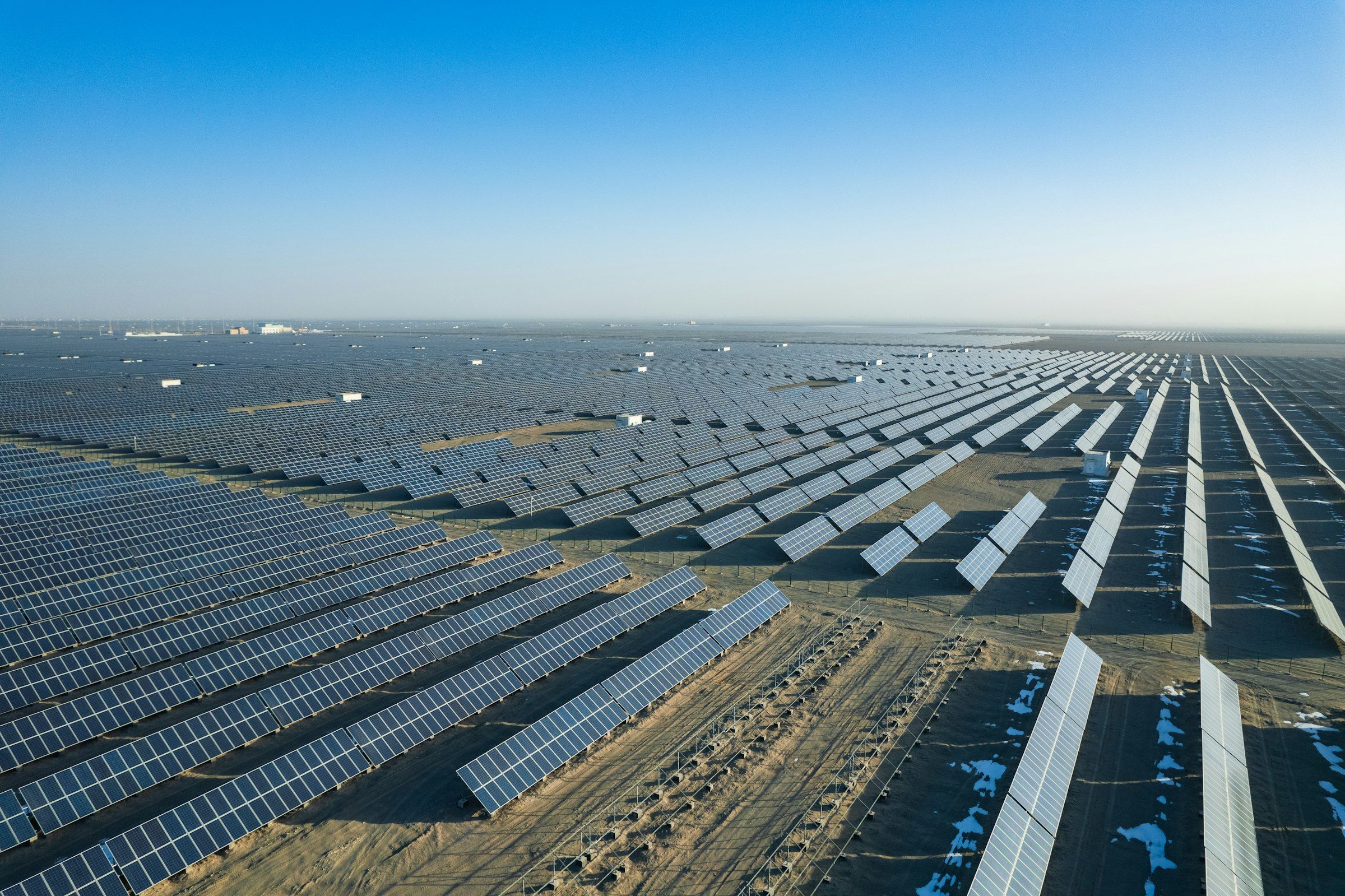 Aerial view of a large solar power plant, with rows of photovoltaic panels stretching across arid ground to the horizon
