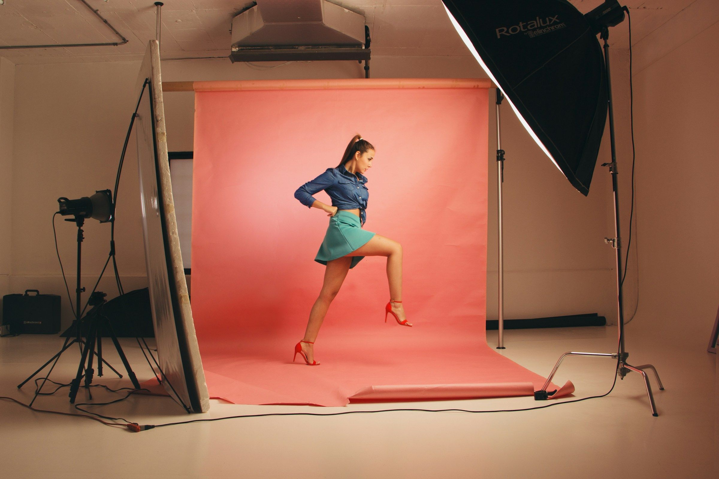A model posing on a pink backdrop in a photography studio, lit by a softbox