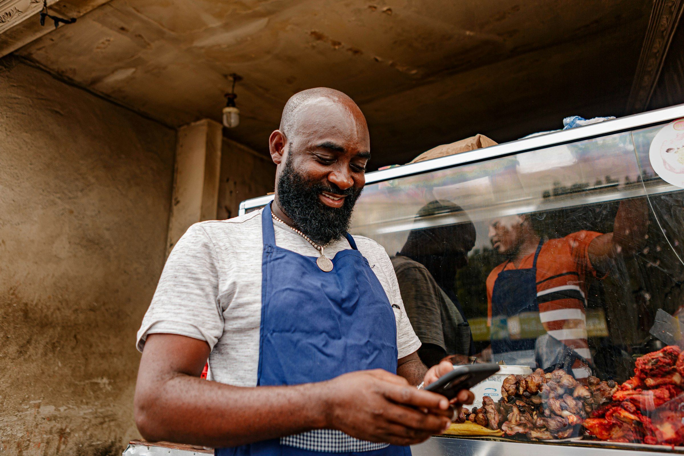 A shop owner in an apron reading a message on his phone
