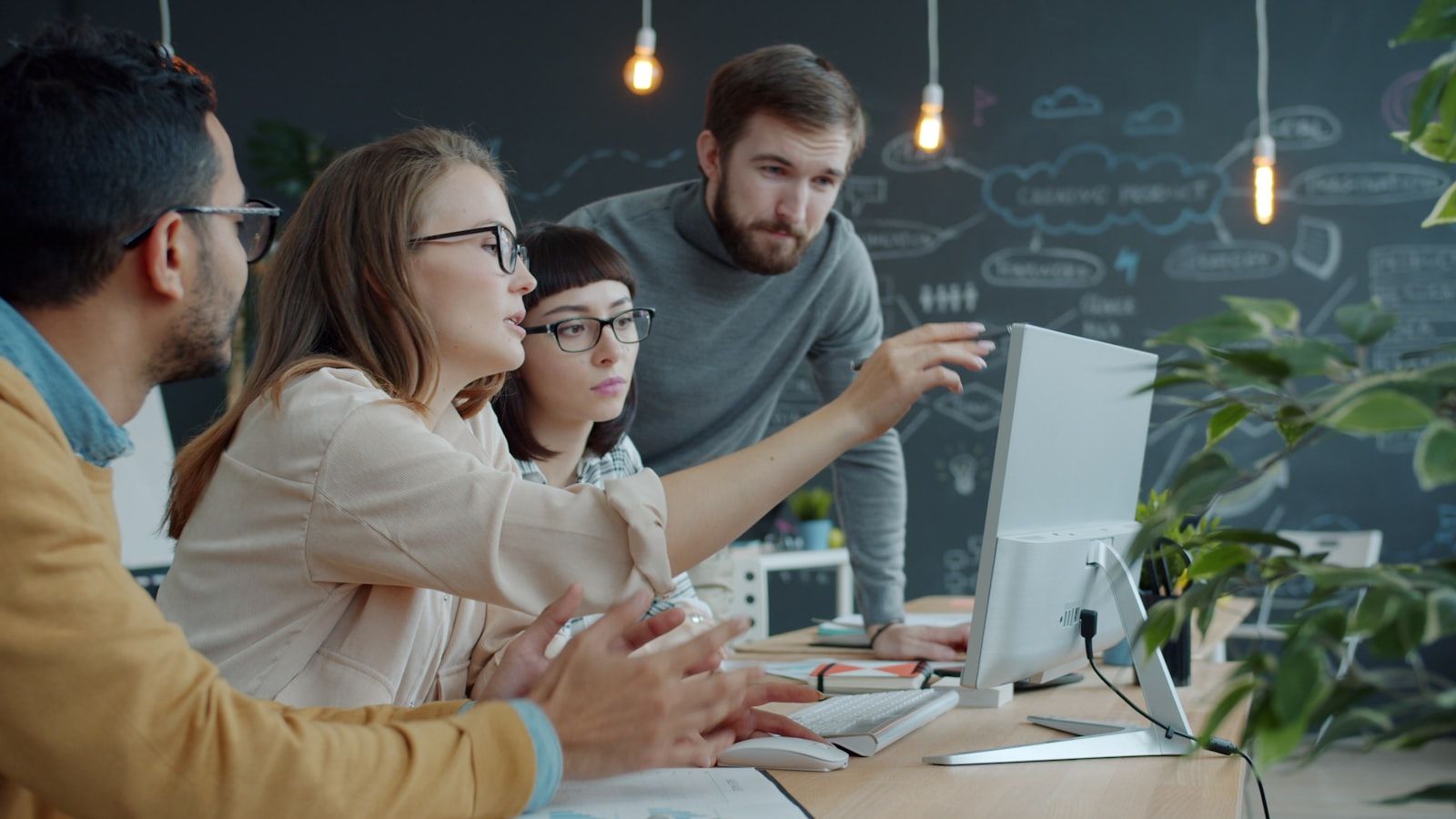 Colleagues gathered around one desktop monitor, one of them pointing at the screen