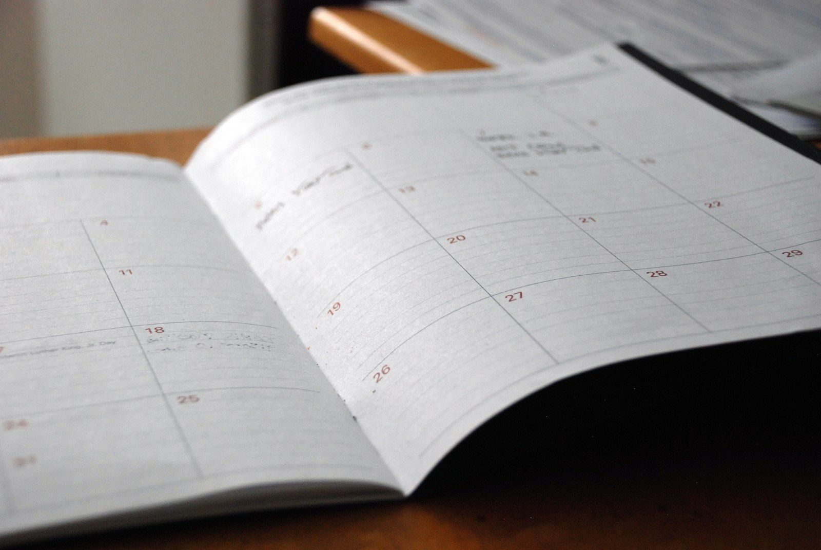 An open monthly paper planner lying on a wooden desk