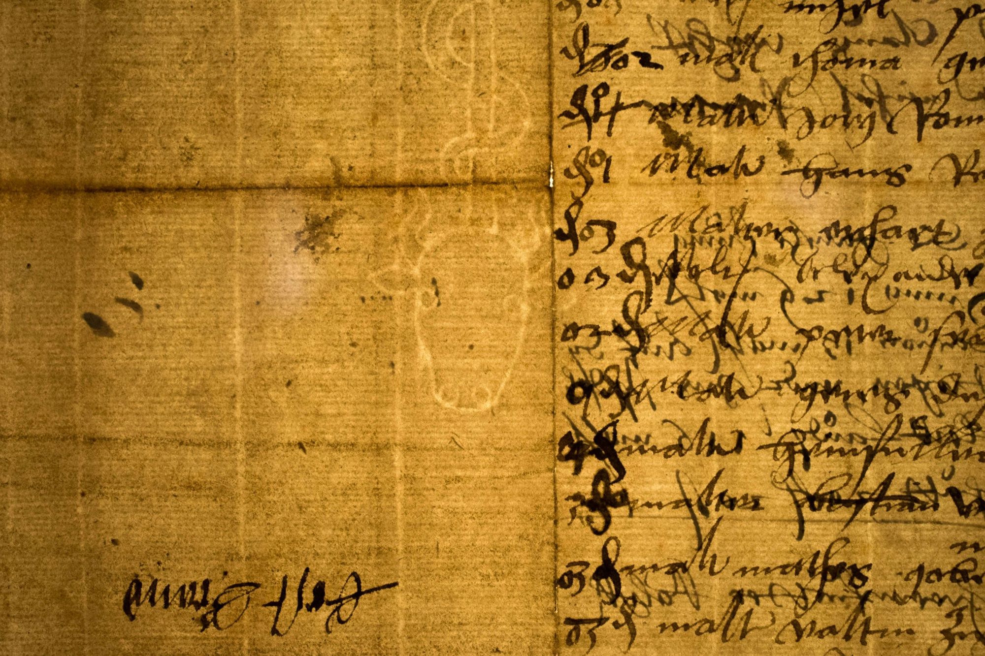 An old folded sheet of laid paper with lines of faded brown handwriting on the right and the faint pale outline of a watermark in the paper on the left