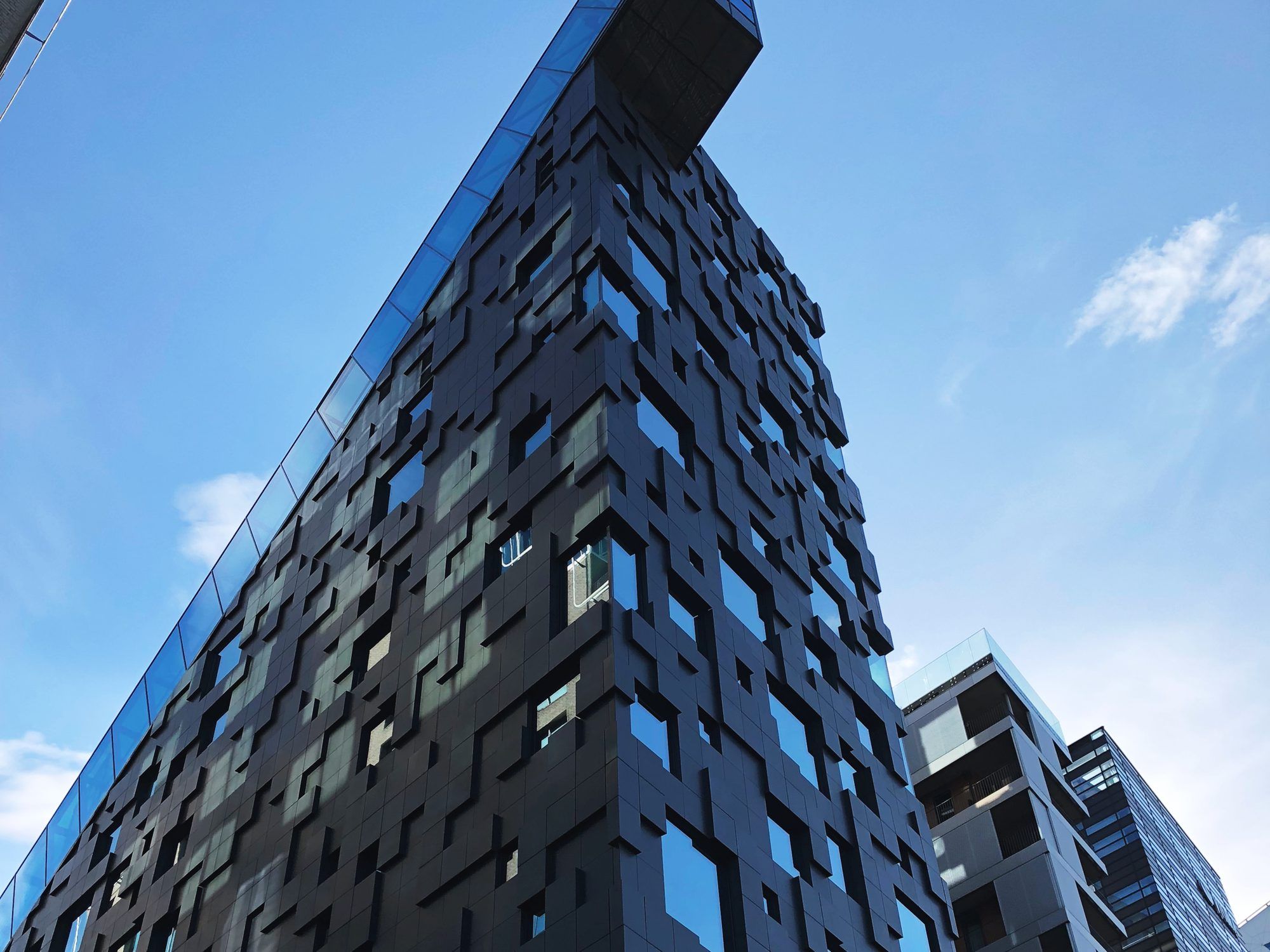 DNB's dark, pixel-patterned office building in Oslo's Barcode district, seen from below against a blue sky