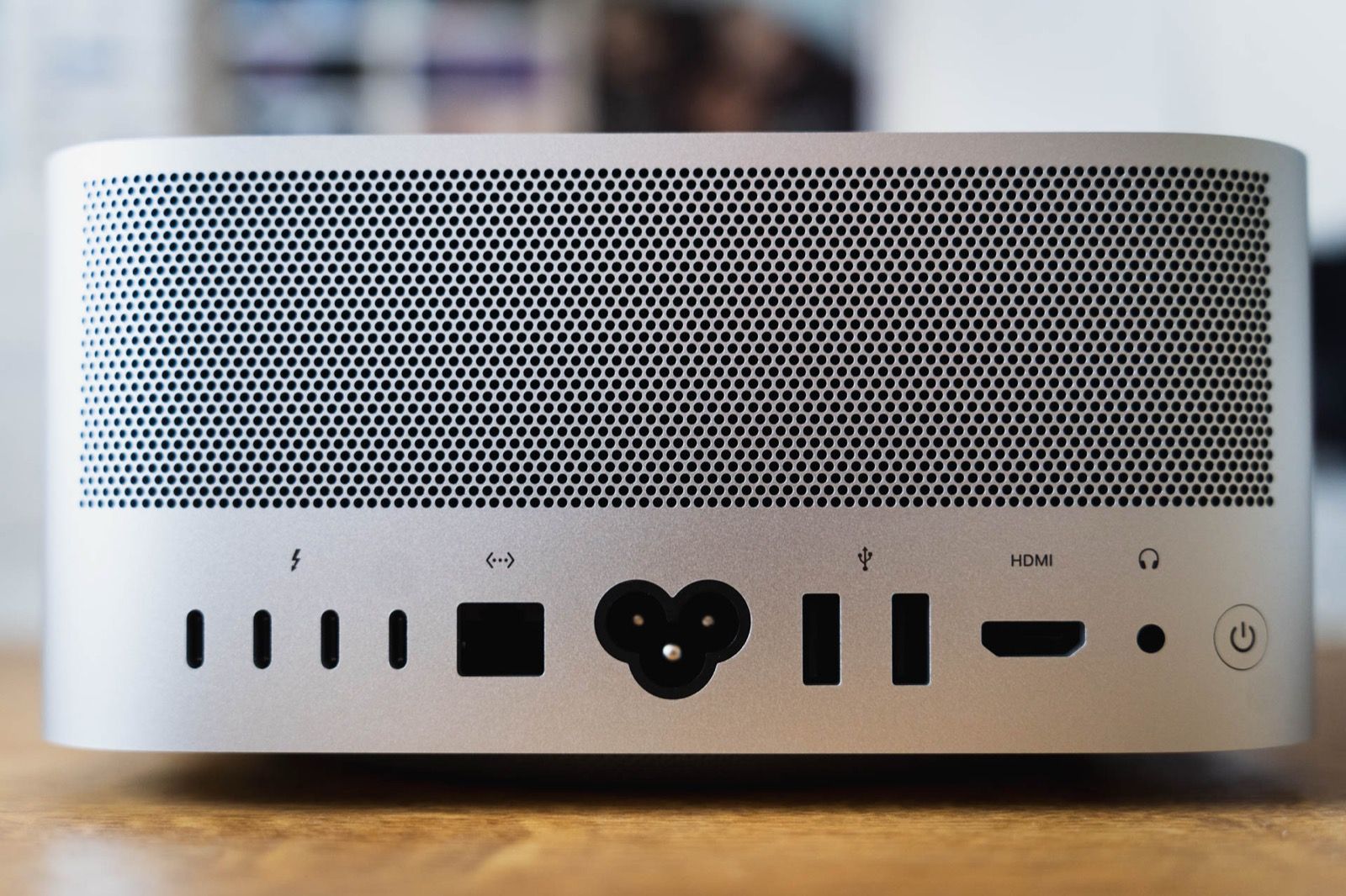 The back panel of an Apple Mac Studio desktop computer on a wooden desk, showing its ports and ventilation grille