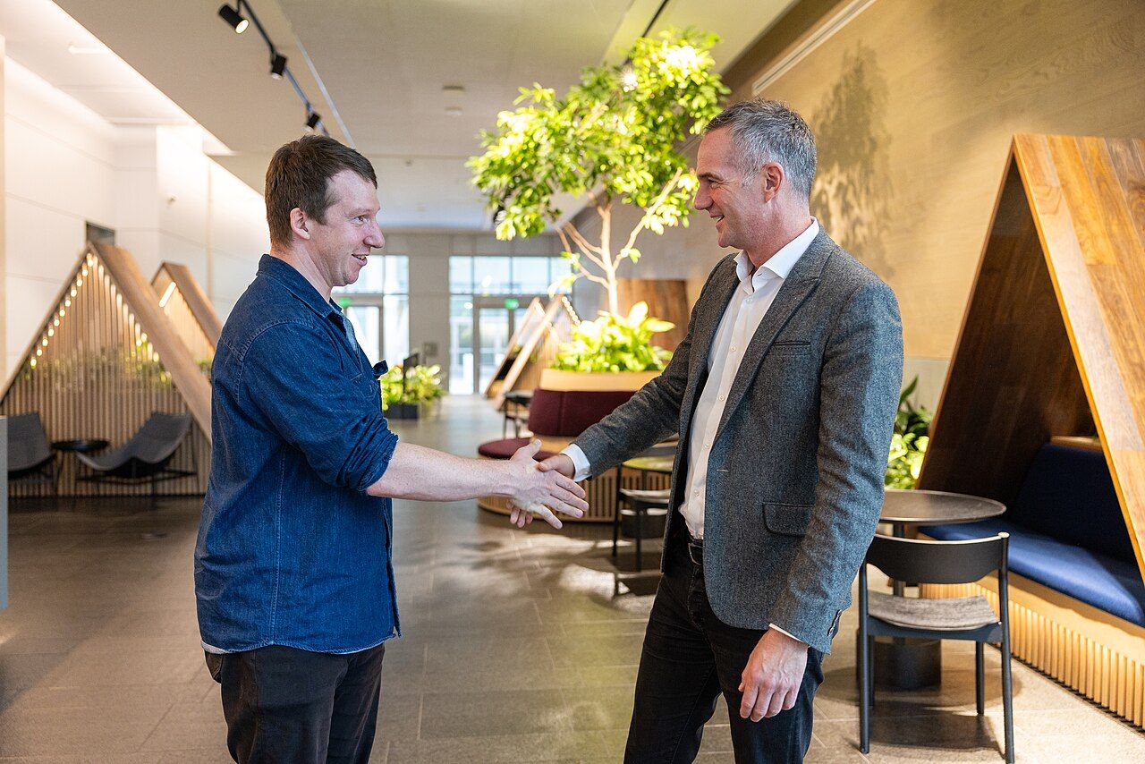 Two men shake hands in a wood-panelled lobby with booth seating and an indoor tree, during UK Science Secretary Peter Kyle's visit to Anthropic in San Francisco in October 2024