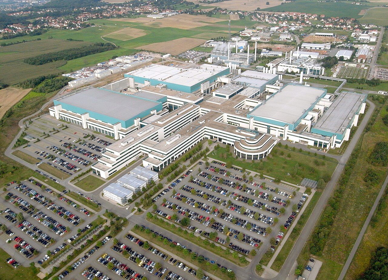 Aerial view of GlobalFoundries' Fab 1 chip plant in Dresden, Germany: large white and teal factory buildings surrounded by car parks and fields