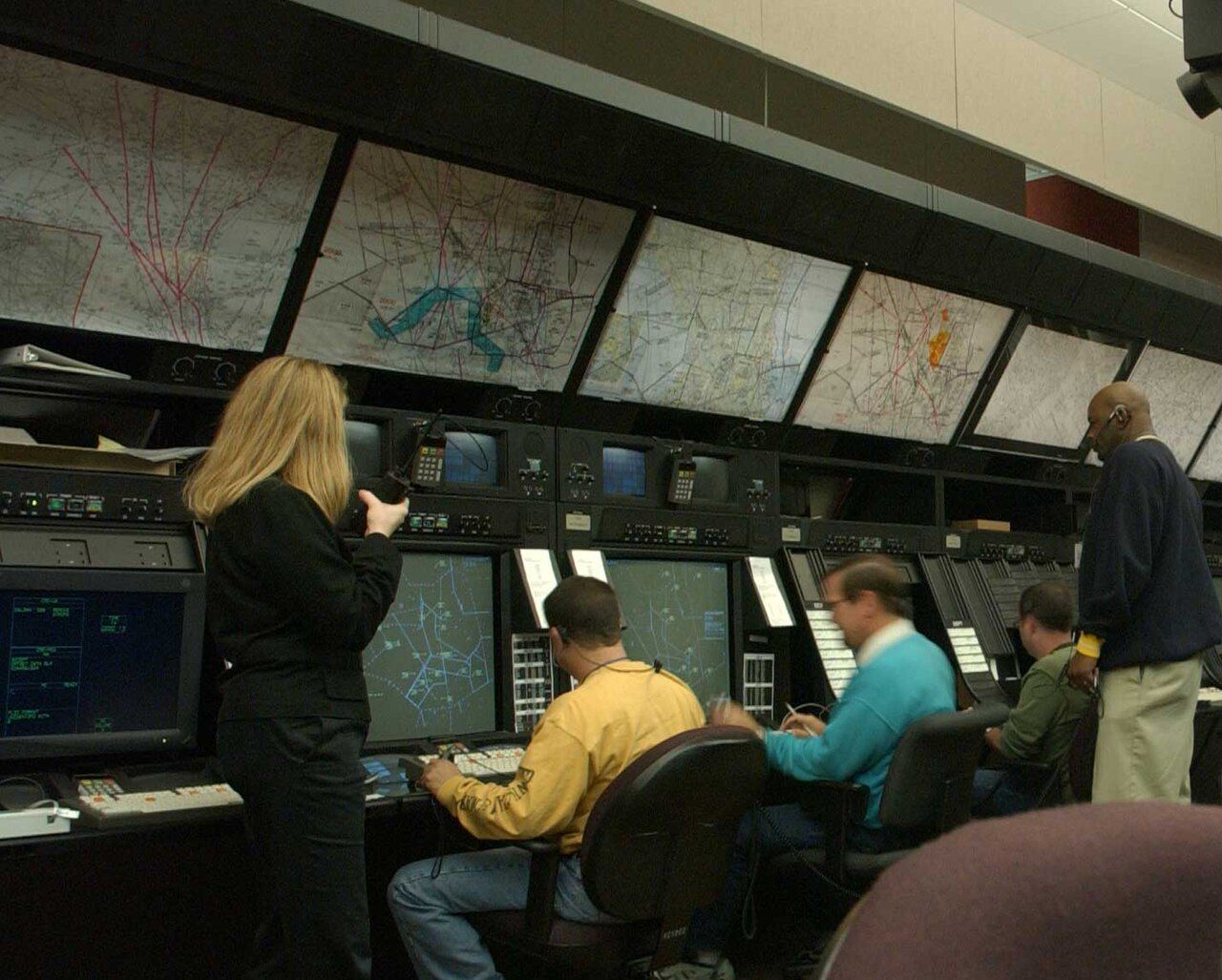 Air traffic controllers at radar screens in the Washington Air Route Traffic Control Center, beneath a row of sector maps