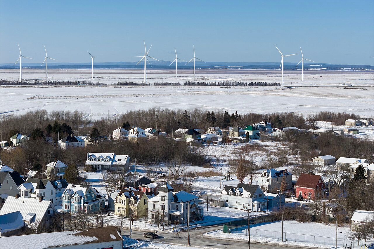 Wind turbines of the Amherst Wind Farm in Nova Scotia stand beyond snow-covered fields, seen over the houses of Amherst in winter